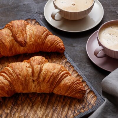 Board with tasty croissants on dark table, closeup. French pastry. Fresh croissant on dark brown mood background, copy space for your product. Close up of pile of delicious croissants on a dark background. Selective focus.