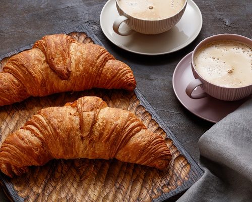 Board with tasty croissants on dark table, closeup. French pastry. Fresh croissant on dark brown mood background, copy space for your product. Close up of pile of delicious croissants on a dark background. Selective focus.